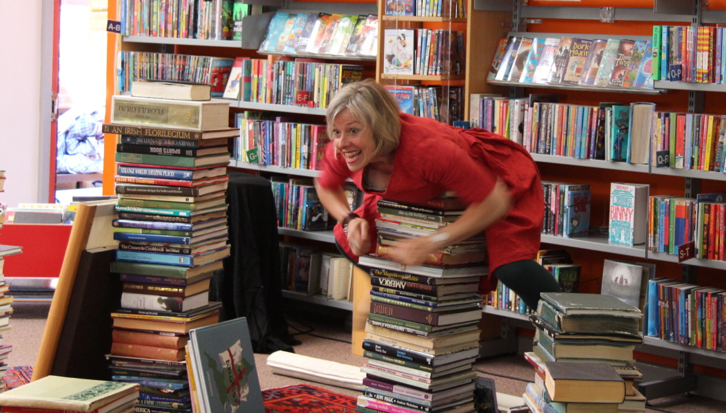 Image of An excited woman climbs on a stack of books in a library